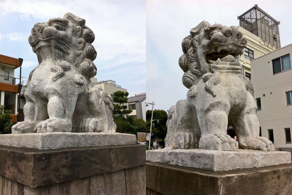 Two stone komainu guardian lion-dogs side by side, one with its mouth open and one with its mouth closed