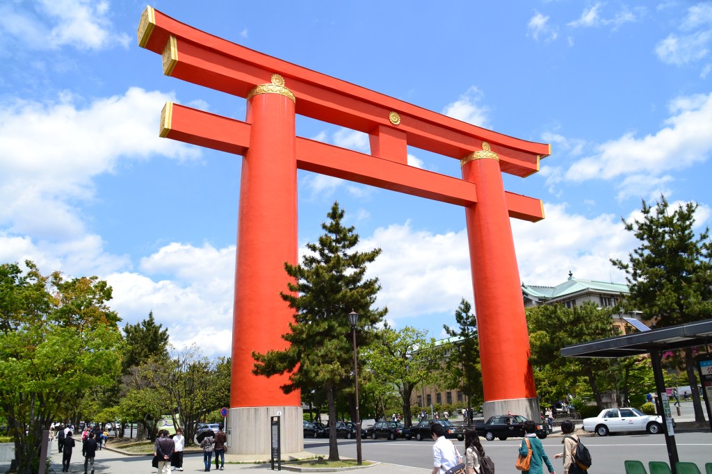 The giant vermilion great torii of Heian Jingu in Kyoto, with a top beam curving upward at the ends, against a blue sky